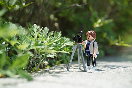 boy plastic toy with tripod camera beside green plant at daytime