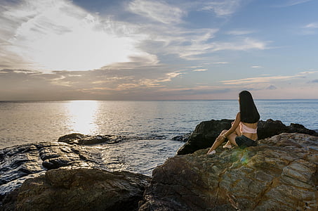 woman sitting near rock formation in front of sea