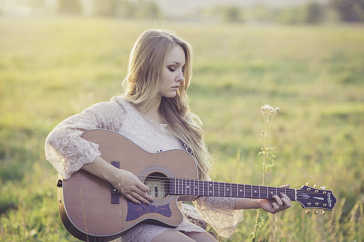 shallow focus photography of woman playing cutaway acoustic guitar