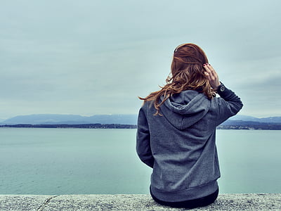 woman wearing gray hoodie overlooking body of water