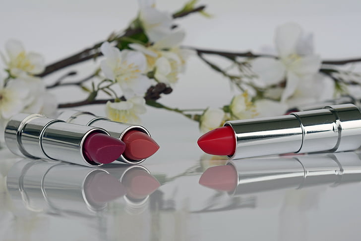 three assorted-shades of lipstick beside white petaled flowers