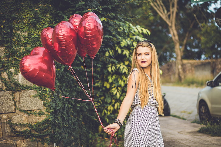 woman holding five heart red balloons