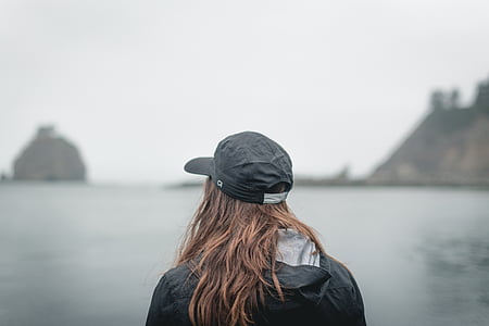 photo of woman in black jacket looking towards islands