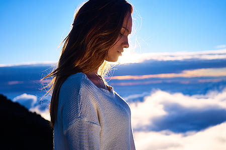 woman in white top standing near clouds on top of mountain