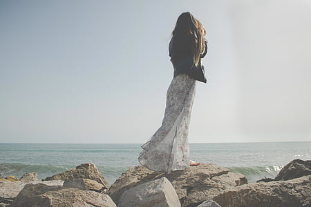 woman standing on stone near ocean