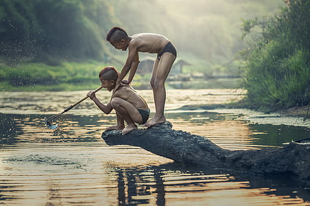 photo of two boys standing on rock on top of body of water