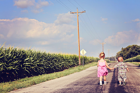 boy and girl holding hands while walking along the road