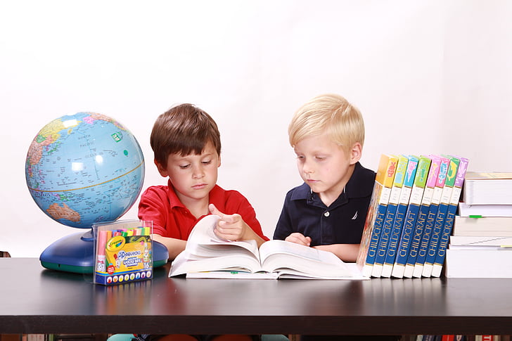 two boys sitting on chair reading book