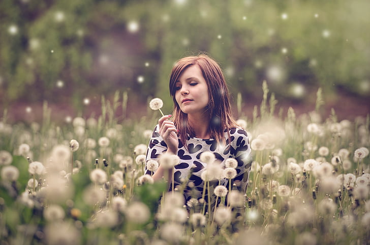 woman wearing white and black heart print top in bed of dandelion flowers selective focus photograph
