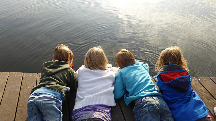 four toddlers in assorted-color jackets planking on brown wooden dock near water during daytime