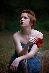woman holding red flower wearing blue sleeveless dress