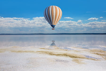 yellow and white hot air balloon above clear water under white clouds and blue sky during daytime
