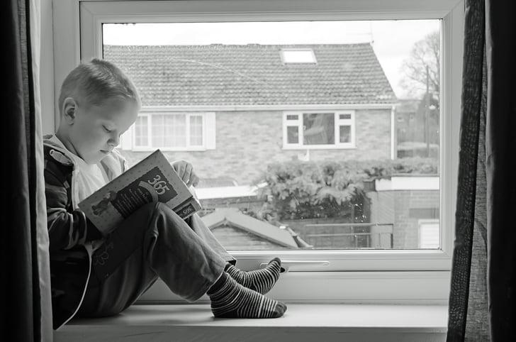 boy sitting on window reading book