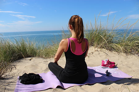 woman sitting on purple yoga mat in front of body of water