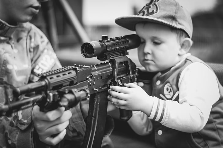 boy wearing flat brim cap holding assault rifle