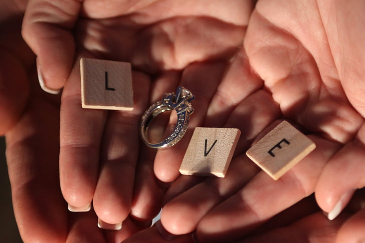 letter L, V, and E scrabble tile and silver-colored diamond stud ring to form a Love word