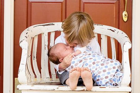 girl kissing the baby while sitting on chair