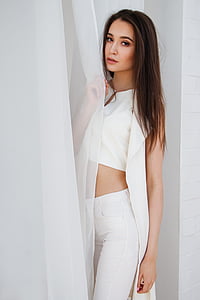woman wearing white split-neck crop top holding white curtain inside white painted room