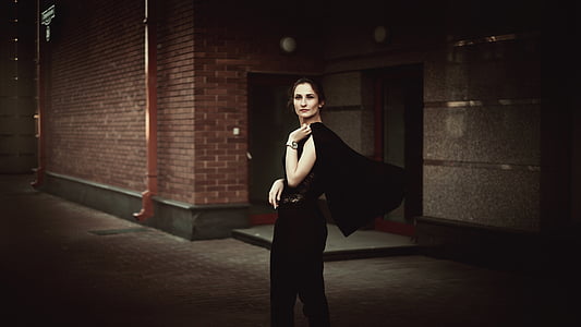 woman wears black sleeveless dress with black scarf near brick building