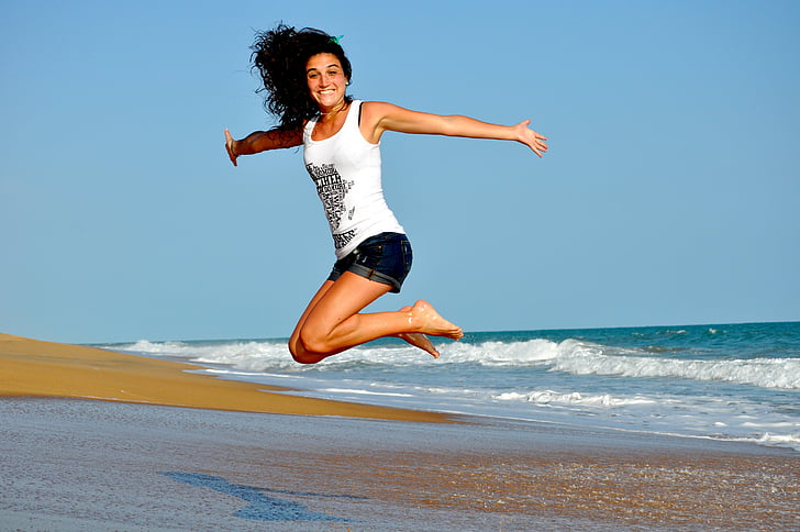 woman wearing white tank top jumping near seashore