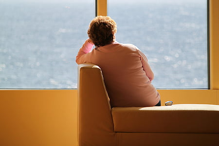 woman sitting on couch facing window pane with view of body of water