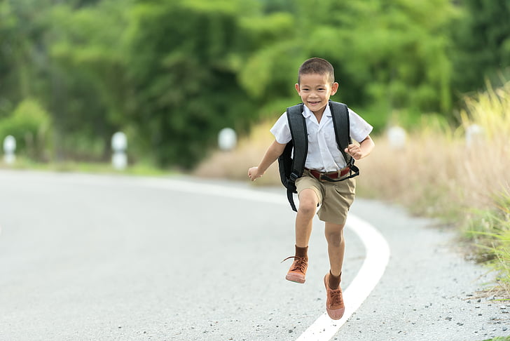 boy carrying backpack walking on road