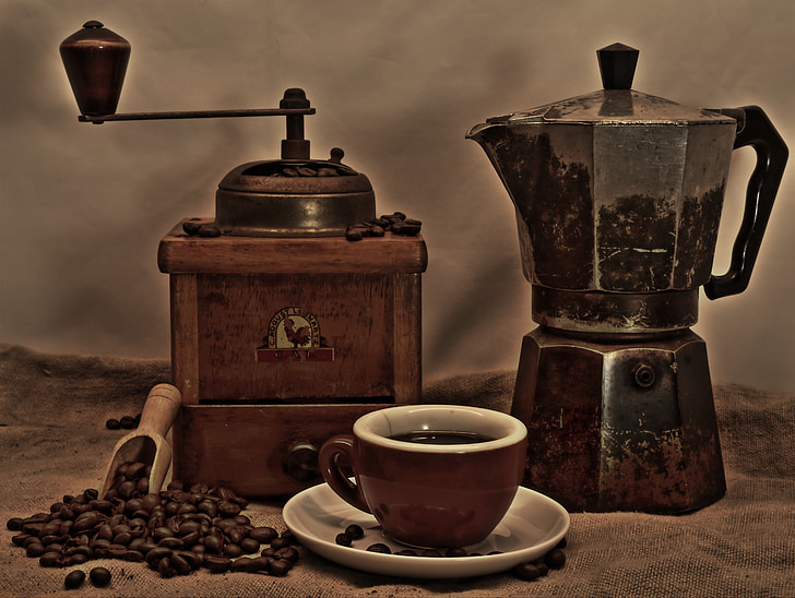 brown manual coffee grinder and black and brown coffee pot behind brown and white ceramic coffee cup