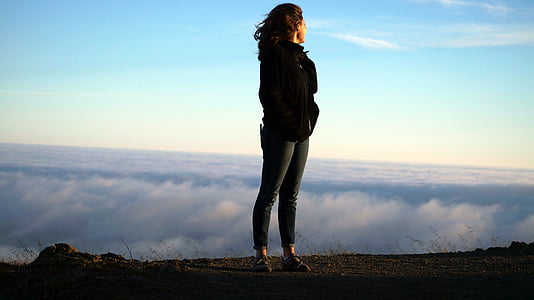 woman standing on hill while while facing white clouds during daytime