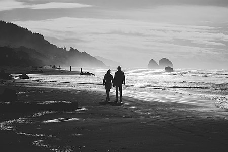 couple walking near body of water greyscale photo
