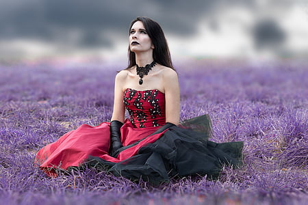 woman wearing red and black strapless dress sits on purple grass field at daytime