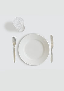round white ceramic plate beside butter knife and fork with clear footed glass
