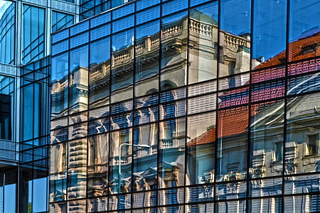 clear curtain wall building with a reflection of gray concrete building taken during daytime