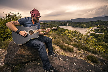 man playing black acoustic guitar sitting on rock