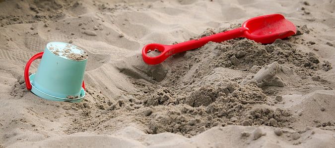 macro photography of blue plastic bucket and red plastic shovel on sand