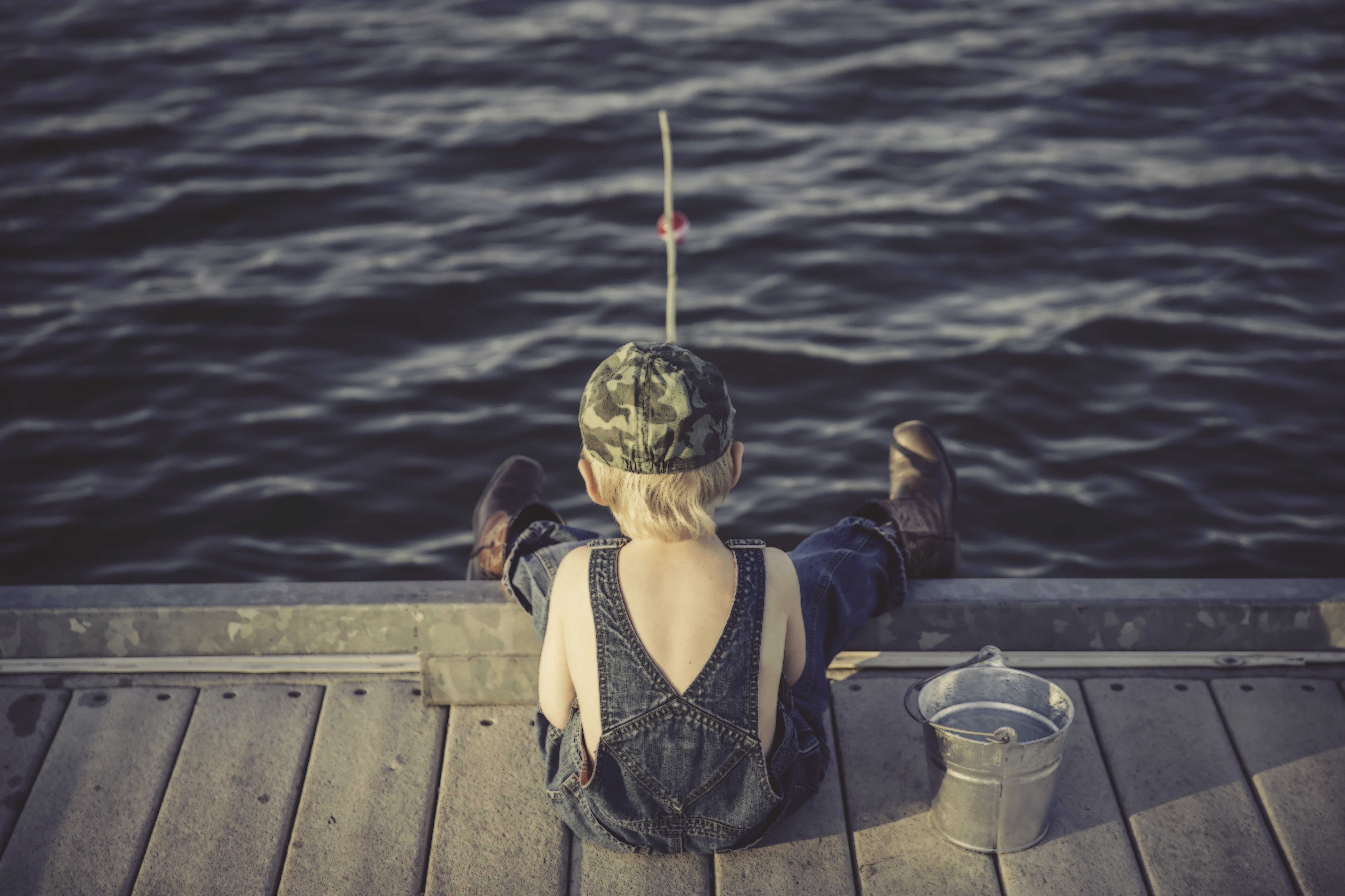 Royalty-Free photo: Boy's wearing fishing wader sitting on the brown dock