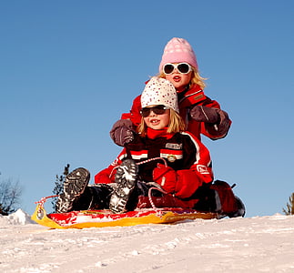 two girls wearing sunglasses riding on yellow and red snow sled during daytime