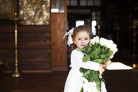 girl in white dress holding white roses bouquet inside a brown room