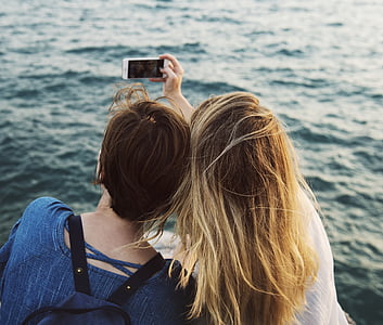 two women taking photo on front of body of water