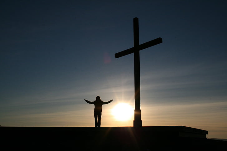 silhouette person standing beside of crucifix statute