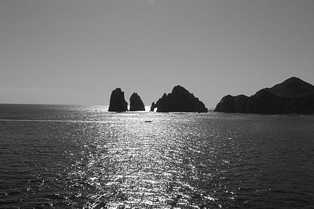 grayscale photo of rock formations surrounded by body of water