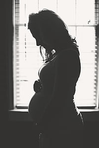 grayscale photography of pregnant woman near window