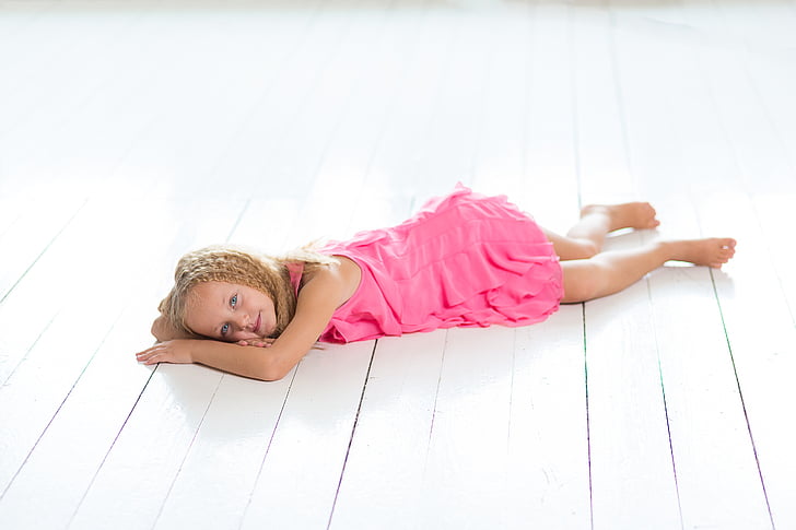 braided blonde girl wearing pink dress lying on floor