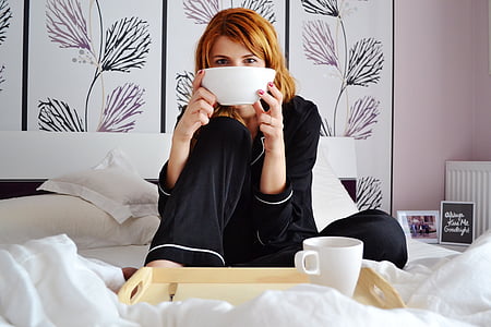 woman in black pajama sitting on bed holding white bowl