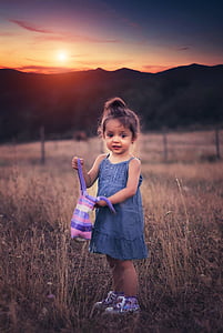 girl wearing blue chambray spaghetti strap dress holding purple striped bag during sunset