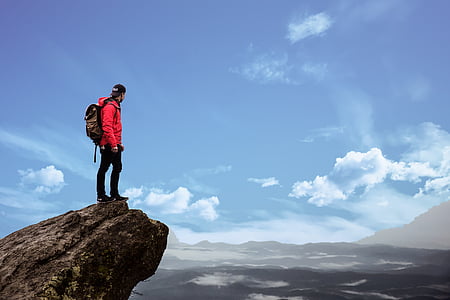 man wears red jacket standing on rock formation at daytime