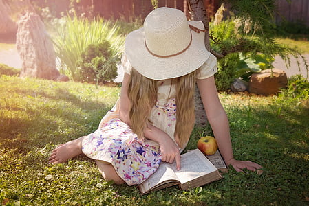 girl with beige hat reading book white sitting on sod