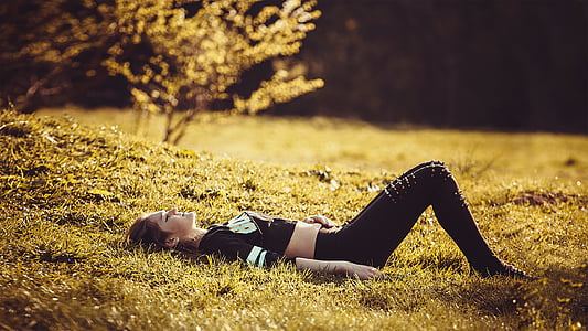 woman in black crop top and black pants lying on green grass during daytime