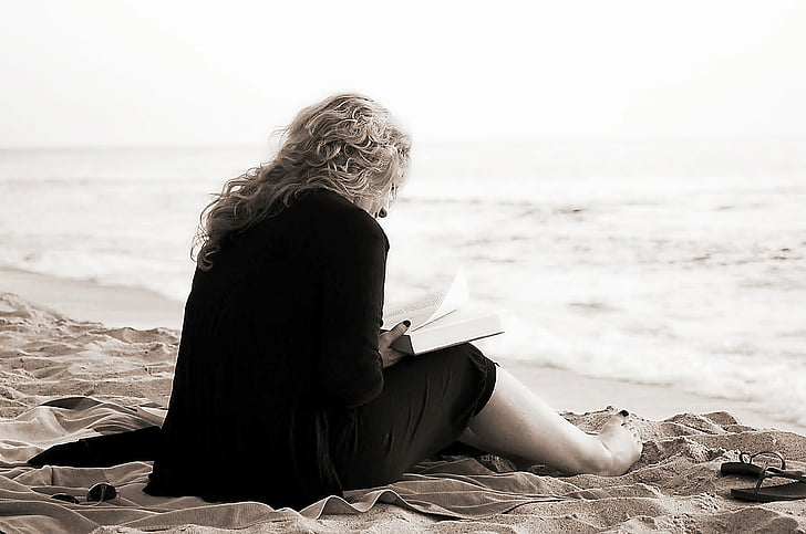 woman sitting on sand reading book