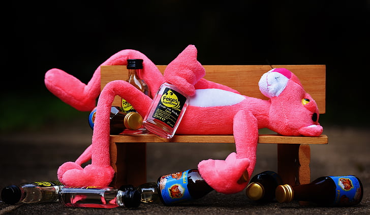 pink panther plush toy laying on brown wooden bench near liquor bottles