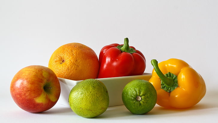 two bell peppers and four fruits on white surface